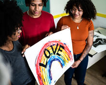 Three teens hold a painting of a rainbow with the word "love" on it.