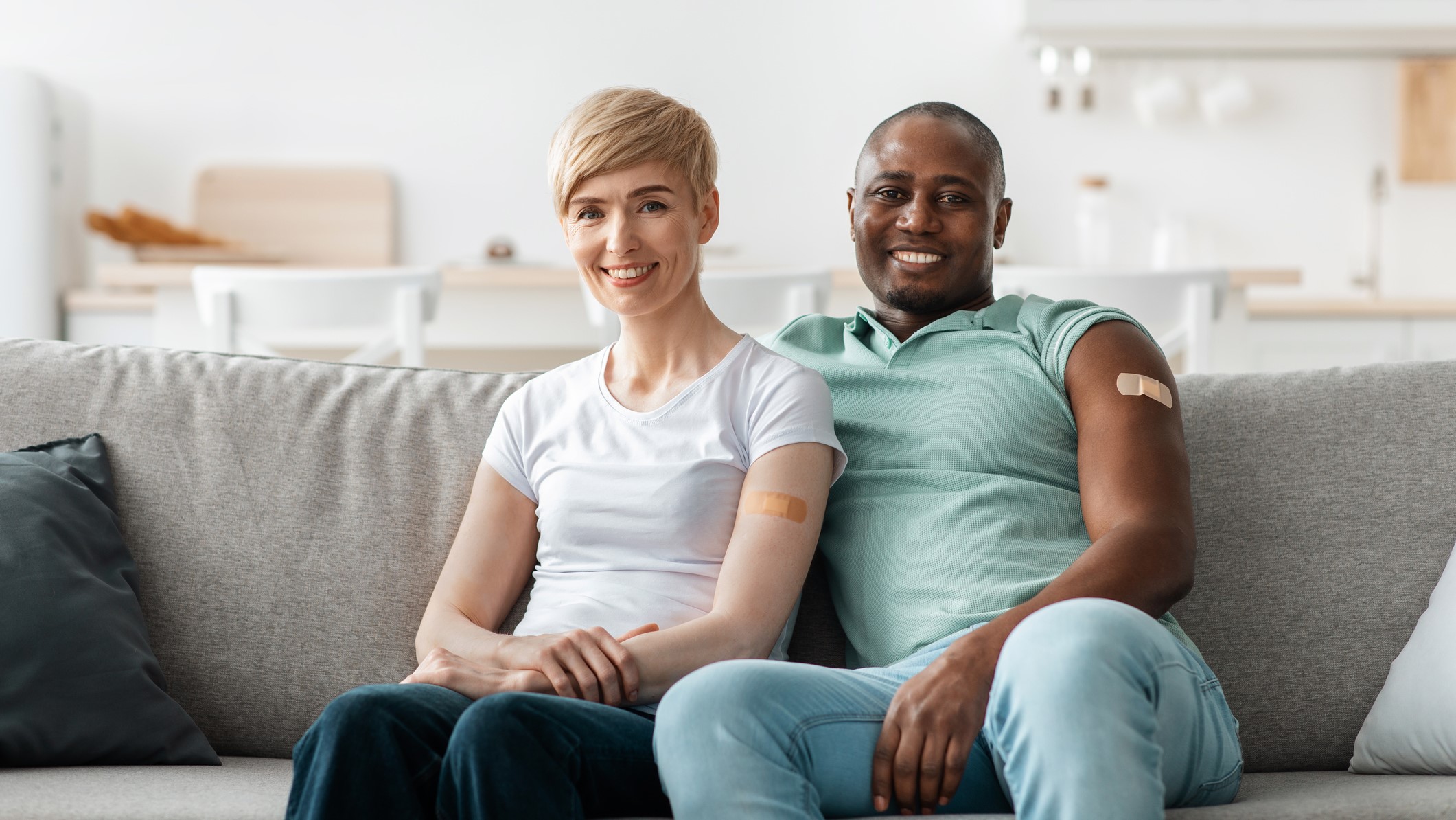 smiling couple sitting on couch with bandaids on their arms