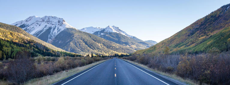 An empty, two-lane road leading to snow-capped mountains in Colorado