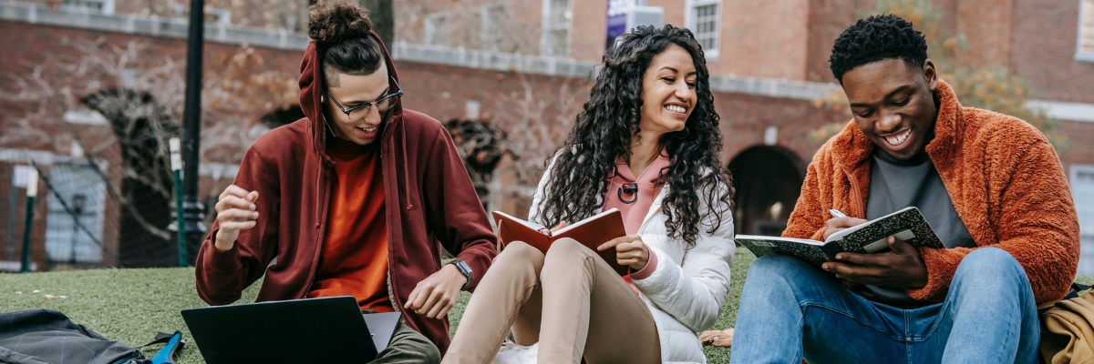 Three students sit on grass at college campus