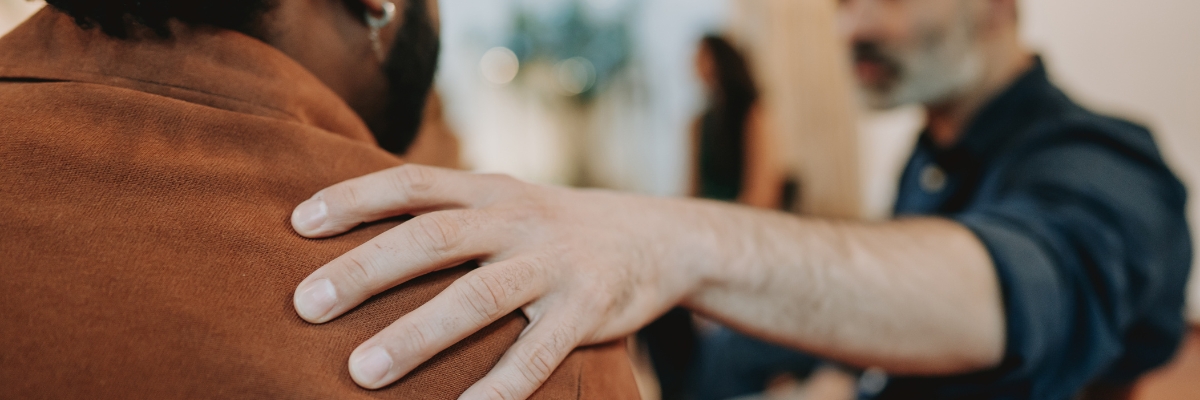 Someone puts a supportive hand on another's shoulder