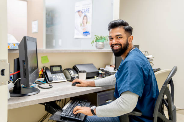 person sitting at a desk with a computer on it, looking at the camera and smiling.
