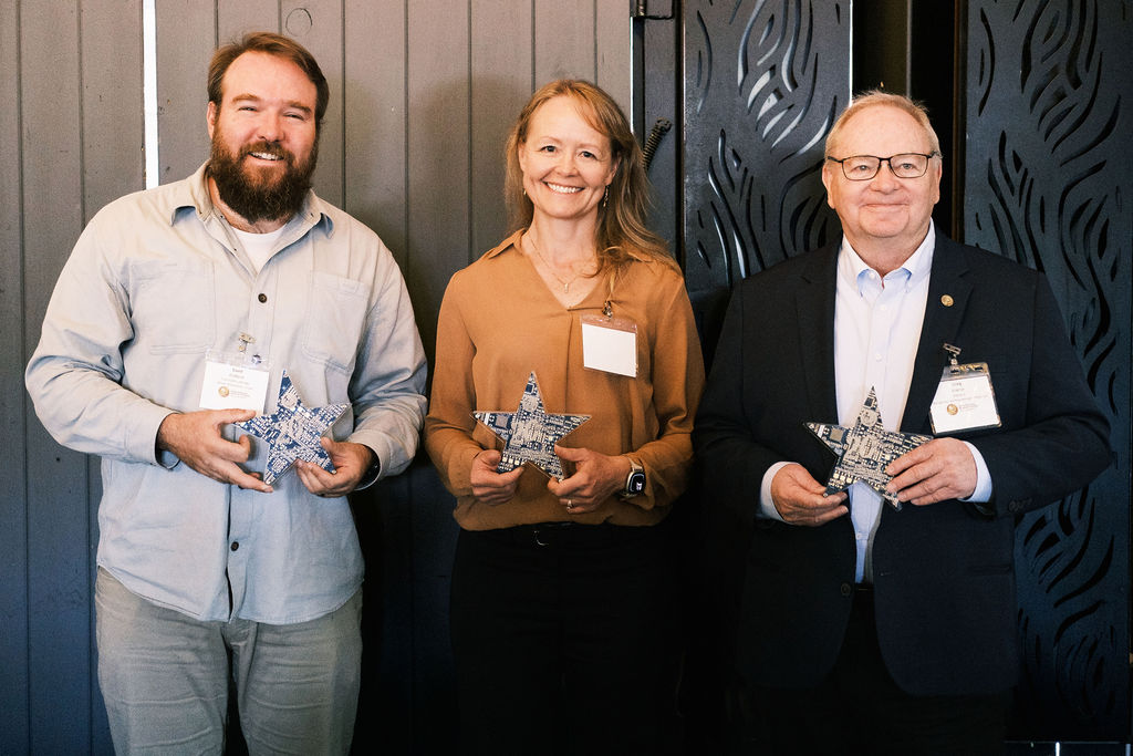 A woman and two men pose for a photo holding star-shaped trophies