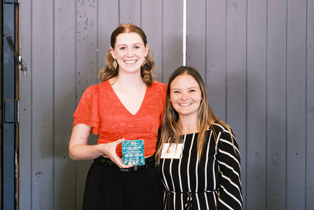 Two woman pose for a photo. The woman on the left is holding a plaque.