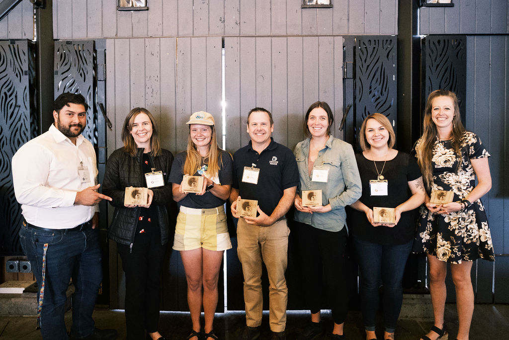A group of seven people pose for a photo holding their award plaques