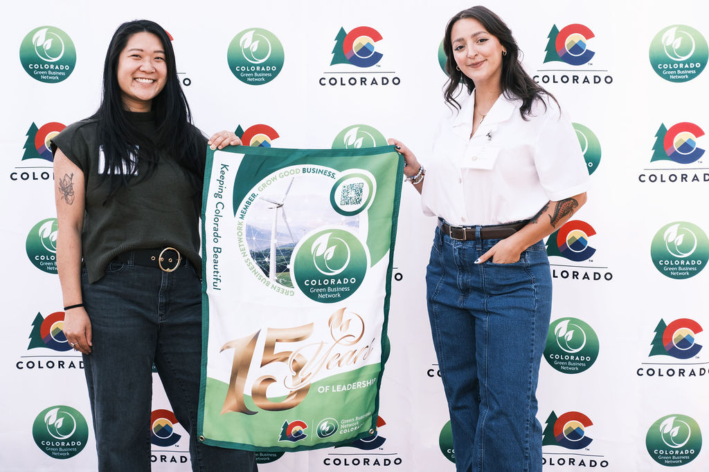 Two women pose for a photo holding banner that displays the message "15 years of leadership"