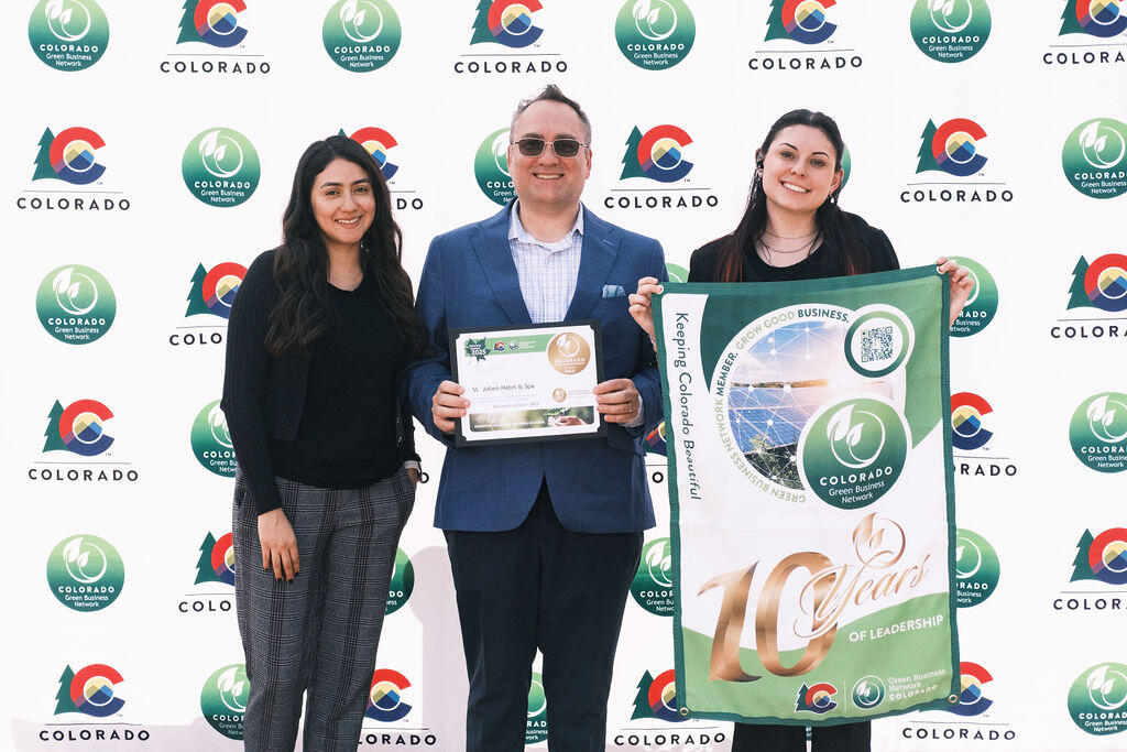 A man and two women pose for a picture. The man holds a certificate and the woman to the right of him holds a CGBN banner with the message "10 years of leadership"