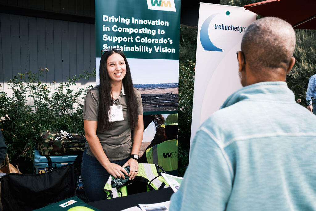 A woman stands behind a table while smiling as a man speaks with her