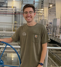 Andrew Canchola standing in a olive green t-shirt smiling. 
