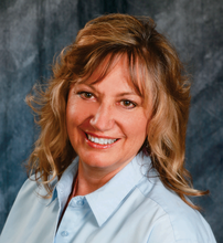 Jan Nelson in a blue shirt with shoulder length short redish /blond hair smiling. 