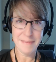 Smiling woman with short brown hair, black wire frame glasses wearing a headset with microphone
