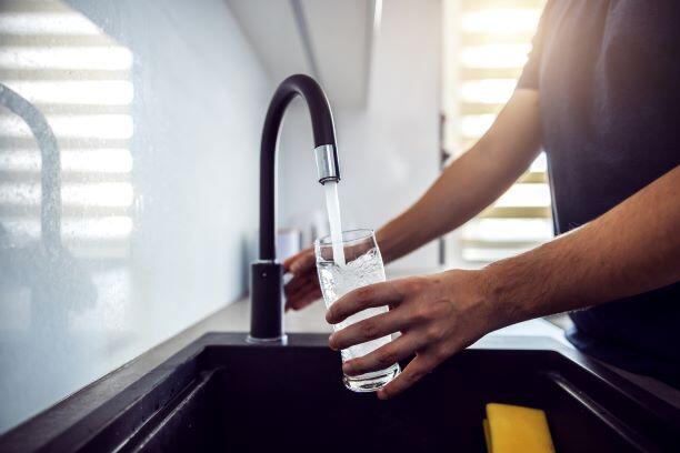 Person filling water glass at kitchen sink.