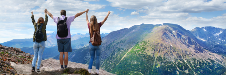 Three hikers raise arms in triumph on Colorado peak, overlooking other mountains