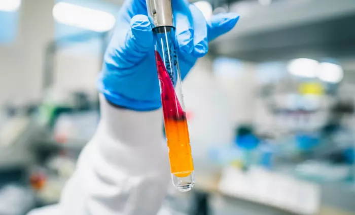 Closeup of someone with lab coat and latex glove holding a colorful test tube. 