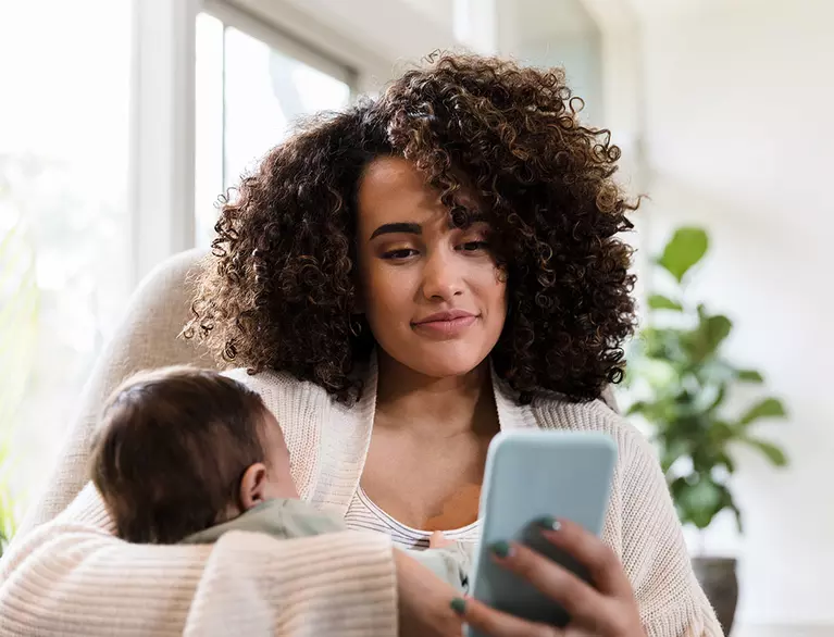  Black mother holding infant and scrolling through smart phone at same time
