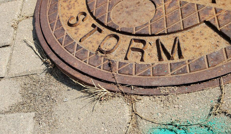 weathered drain cover with the word "storm" raised for identification