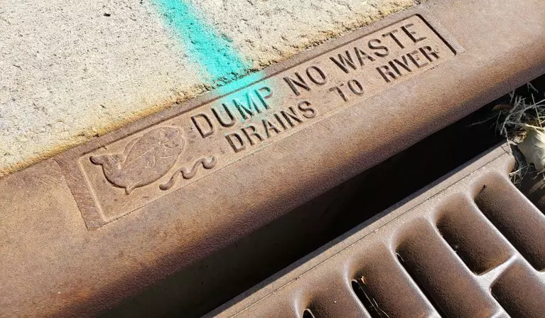 Storm drain with image of fish and the words "Dump no waste drains to river"