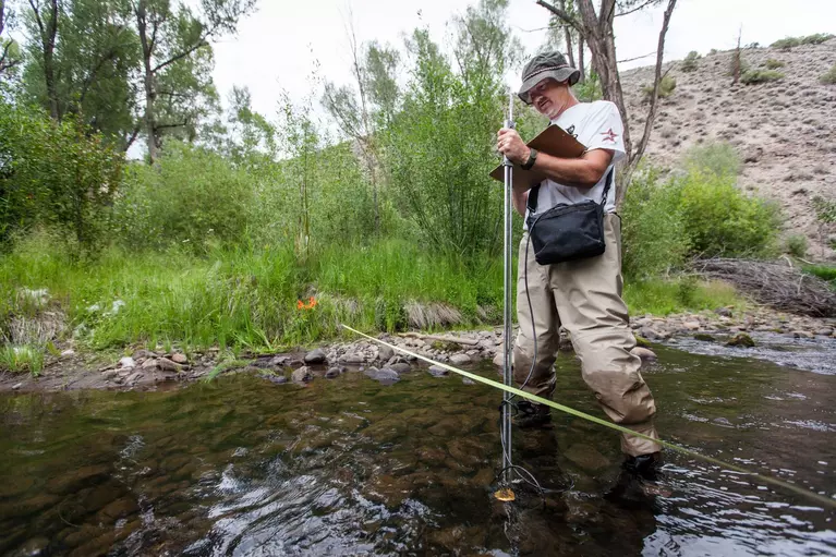 Scientist standing in stream, taking measurements for data