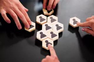 Hands assembling wooden puzzle pieces with people icon on each one.