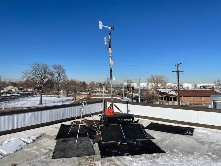 Stationary monitoring site located on a roof top, includes solar panels, a protective case to hold the instrument, and a meteorological station for measuring wind speed and direction