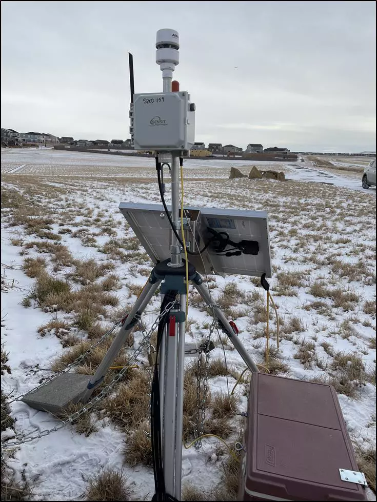SPOD mounted on a tripod in a field near residential area, a solar panel and battery as well as a meteorological station for wind speed and directions data