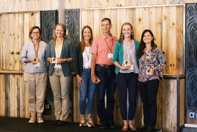 The six 2023 Innovation Spotlight Award winners stand next to each other with their wooden awards in hand.