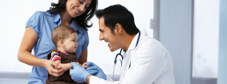 Provider smiling at infant patient that is sitting in parent's lap